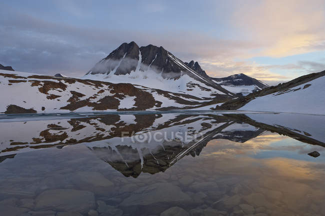 Snowcapped mountains and sunset sky reflecting in lake — Stock Photo