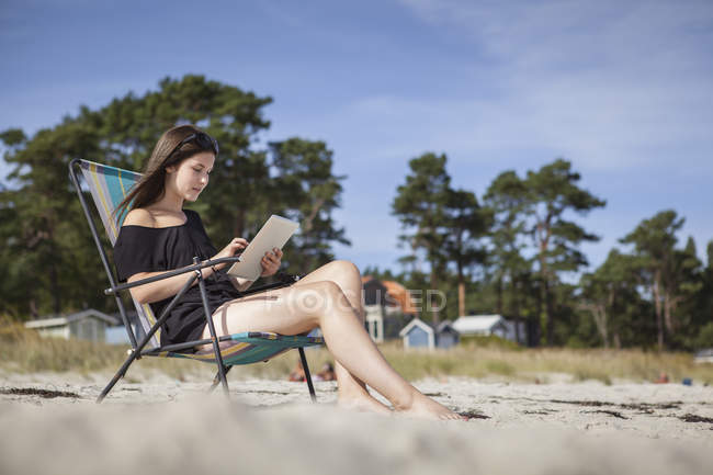 Дівчина-підліток використовує цифровий планшет на пляжі — стокове фото