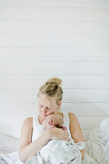 Mulher adulta média segurando bebê menino nos braços contra a parede branca — Fotografia de Stock