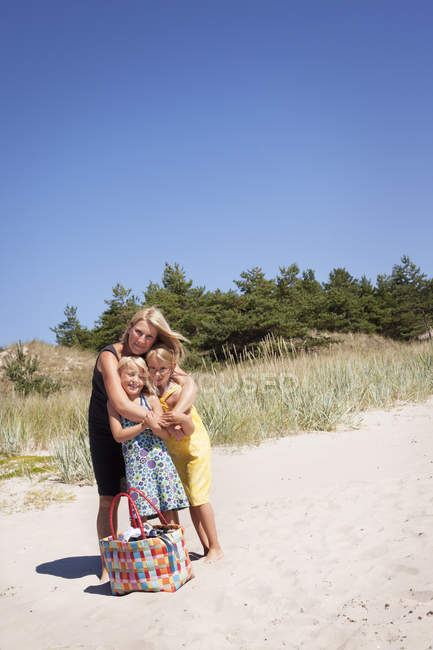 Madre abrazando a dos hijas en la playa - foto de stock