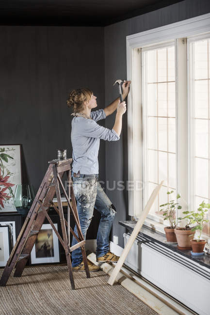 Mujer de mediana edad martillando clavos en la sala de estar - foto de stock