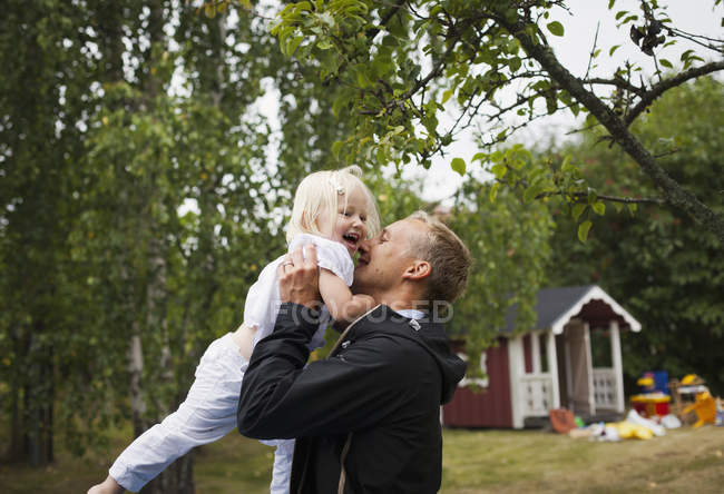 Padre levantando a su hija contra los árboles, concéntrate en el primer plano - foto de stock