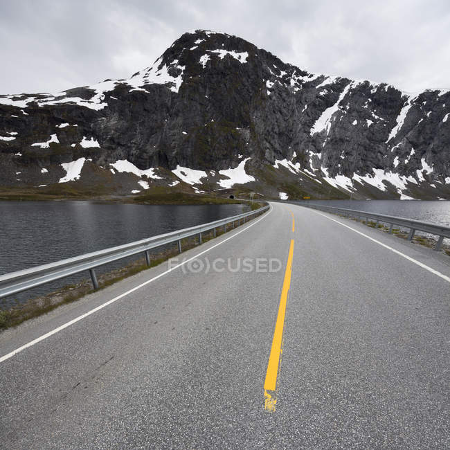 View of road leading over lake to mountain range — Stock Photo