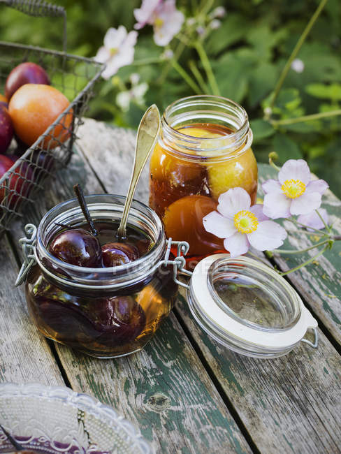 Preserved plums in jars on rustic table — Stock Photo