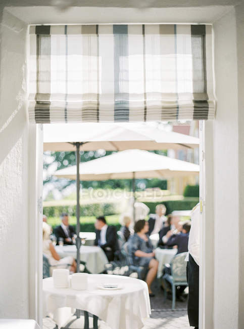 Personas sentadas bajo sombrillas en el restaurante al aire libre - foto de stock