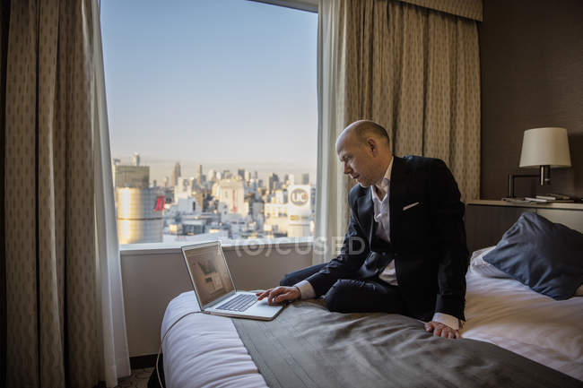 Empresario trabajando en laptop en habitación de hotel con paisaje urbano de Tokio en ventana - foto de stock