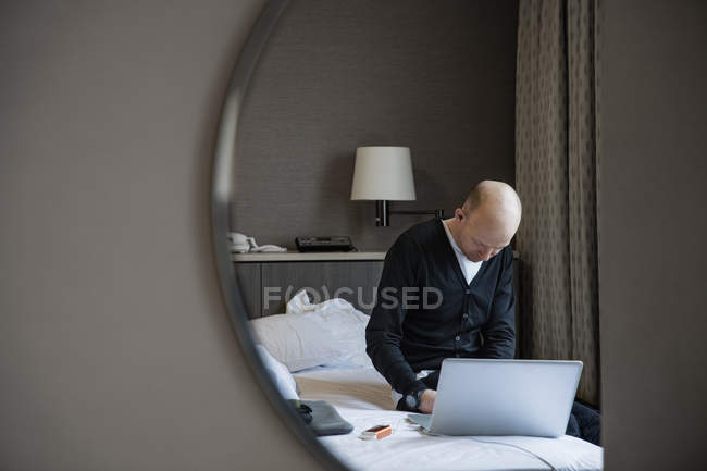 Чоловік сидить на ліжку і використовує ноутбук — стокове фото
