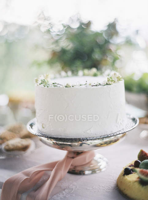 White cake on cake stand with pink ribbon — Stock Photo
