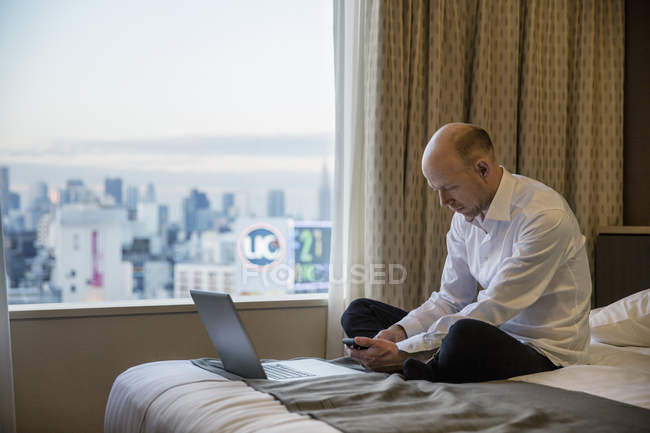 Homme d'affaires utilisant un smartphone dans une chambre d'hôtel avec Tokyo paysage urbain dans la fenêtre — Photo de stock