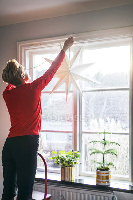 Mature woman hanging Christmas star in window — Stock Photo