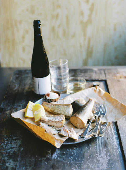 Peixe fumado, limão, talheres e garrafa de vinho na mesa de madeira — Fotografia de Stock