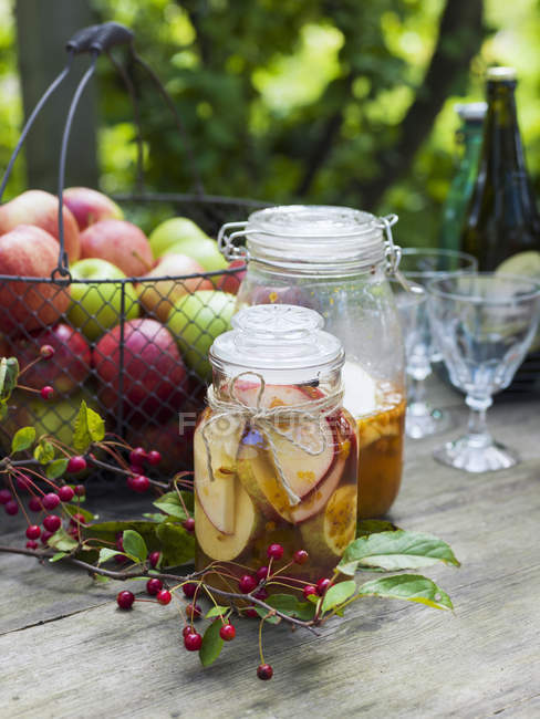 Preserved apples in jars and fresh apples in metal basket — Stock Photo