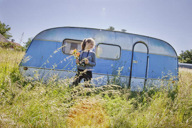 Adolescente en face de remorque de voyage dans l'herbe — Photo de stock