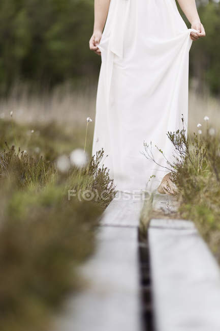 Teenage girl in white dress standing on overpass in meadow — Stock Photo