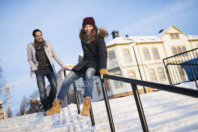 Mann beobachtet junge Frau beim Rutschen am Geländer — Stockfoto