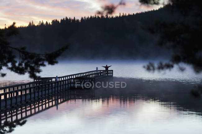 View of lake at sunset with silhouette of person on pier — Stock Photo
