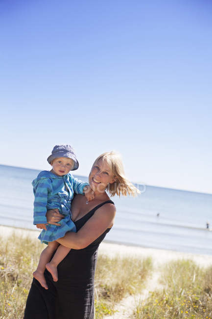 Woman holding son on beach, focus on foreground — Stock Photo