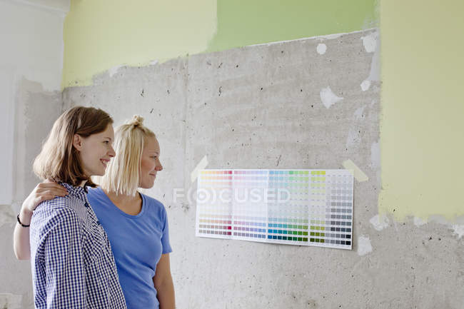 Mujeres jóvenes mirando muestras de color pegadas a la pared - foto de stock