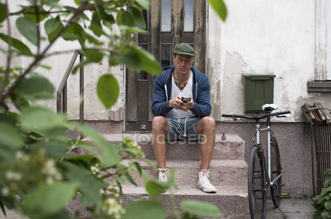 Мужчина сидит на крыльце и пользуется мобильным телефоном — стоковое фото
