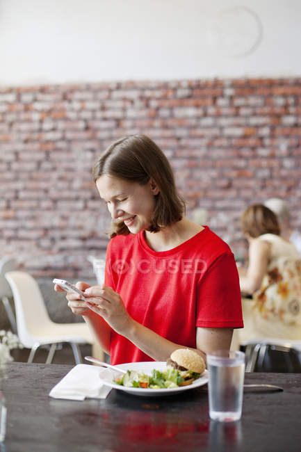 Усміхнена жінка перевіряє смартфон на обід — стокове фото