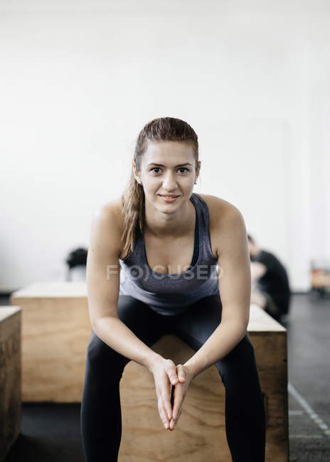 Портрет молодої жінки, що сидить на дерев'яній ящику в спортзалі — стокове фото