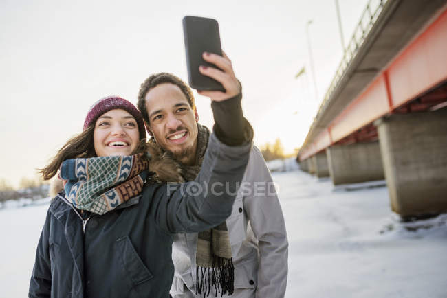 Jeune couple prenant selfie par pont en hiver, se concentrer sur le premier plan — Photo de stock