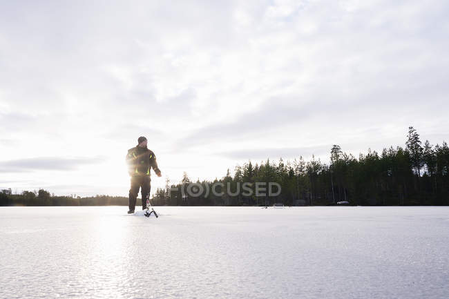 Uomo che si prepara per la pesca sul ghiaccio sul lago congelato — Foto stock