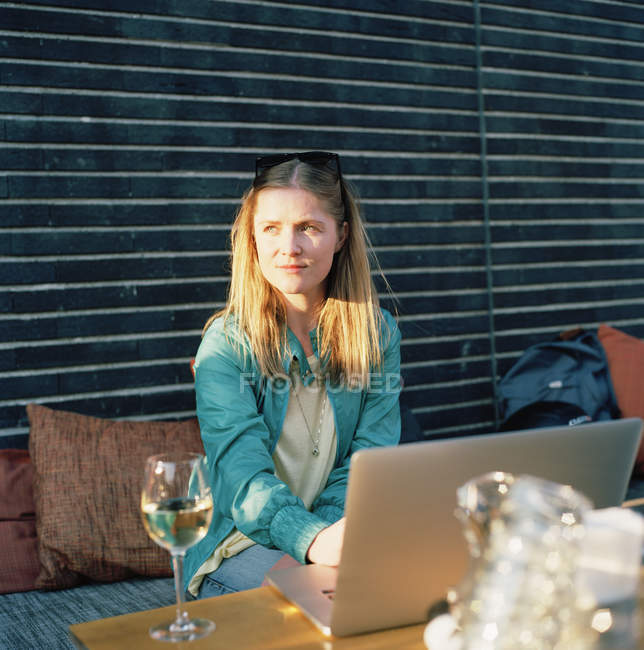 Mulher com copo de vinho branco usando laptop no terraço de verão, foco em primeiro plano — Fotografia de Stock