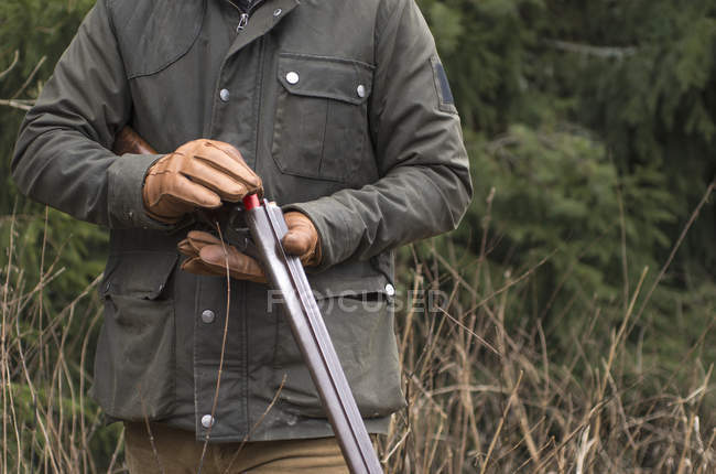 Средняя часть человека заряжает пистолет в лесу — стоковое фото