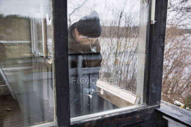 Mann baut Holzgeländer, Blick aus Fenster — Stockfoto