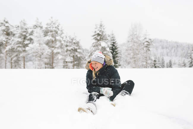 Lachende junge Frau sitzt im Schnee — Stockfoto