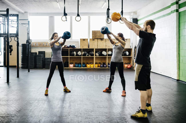 Jovens mulheres e homem balançando kettlebells no ginásio — Fotografia de Stock