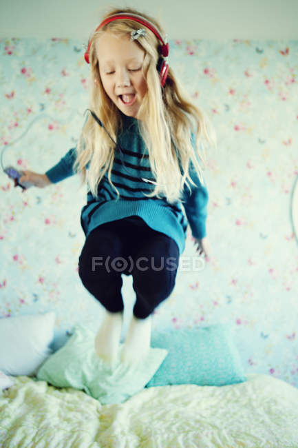 Girl listening to music on headphones and jumping on bed — Stock Photo
