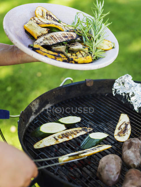 Hombre sosteniendo verduras a la parrilla en el plato y cocinar - foto de stock