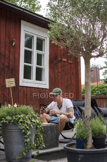Человек сидит на заднем дворе и использует мобильный телефон — стоковое фото