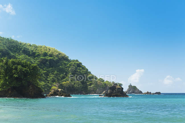 Turquoise sea water with green hill and rock formations under blue sky — Stock Photo