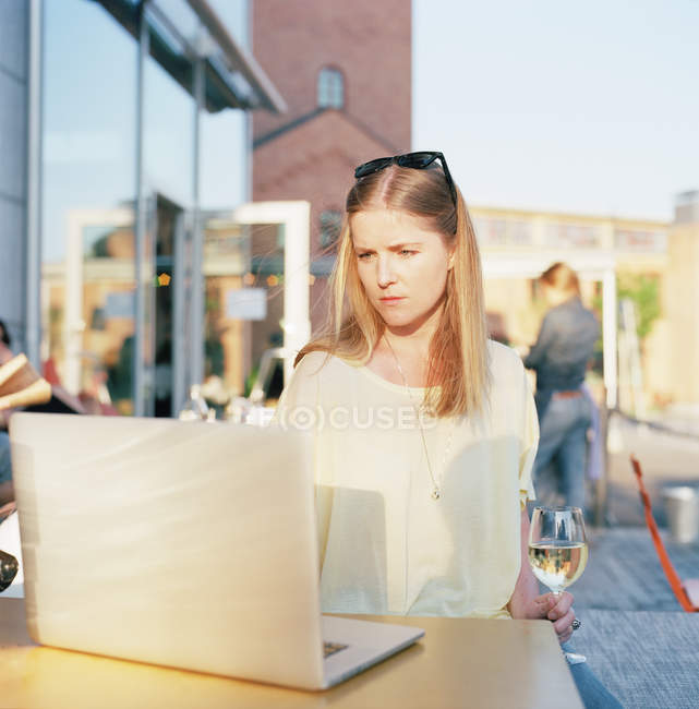 Mulher com copo de vinho branco usando laptop no terraço de verão, foco em primeiro plano — Fotografia de Stock