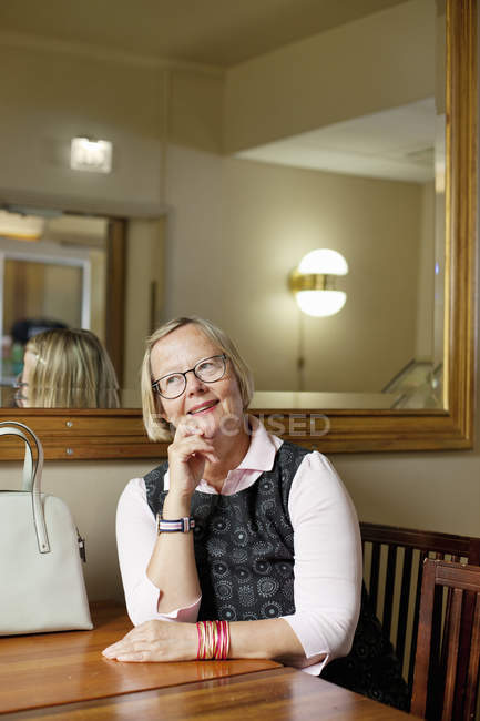 Улыбающаяся пожилая женщина смотрит в сторону и сидит за столом — стоковое фото