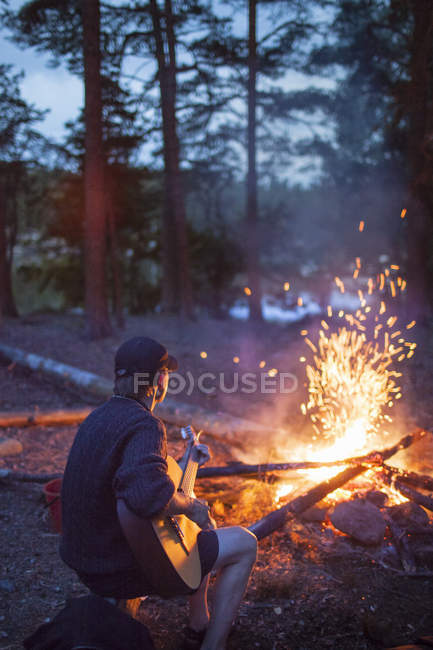 Homem tocando guitarra pela fogueira, foco em primeiro plano — Fotografia de Stock