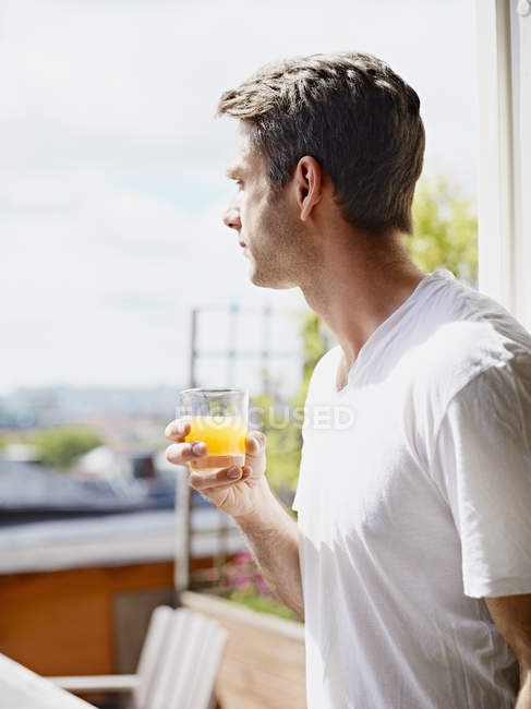 Uomo in possesso di tazza di succo d'arancia alla luce del sole — Foto stock