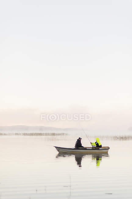 Jeunes hommes pêchant dans le lac au coucher du soleil — Photo de stock