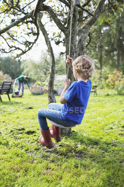 Junge auf Baumschaukel, Mann im Hintergrund, Fokus auf Vordergrund — Stockfoto