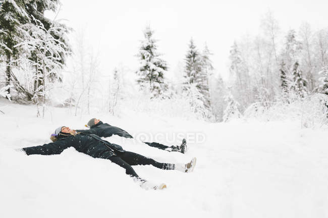 Casal jovem fazendo anjos da neve, foco em primeiro plano — Fotografia de Stock