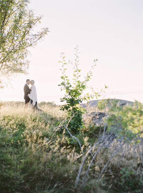 Bride and groom standing face to face in grass, selective focus — Stock Photo