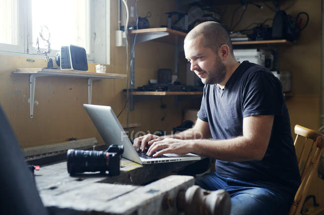 Людина сидить за столом і за допомогою ноутбука — стокове фото