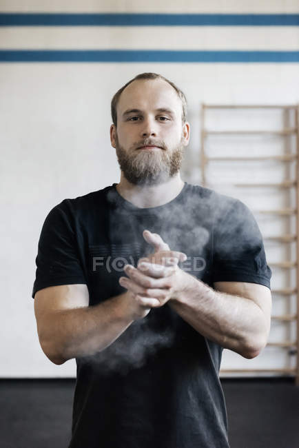 Bearded man chalking hands in gym — Stock Photo