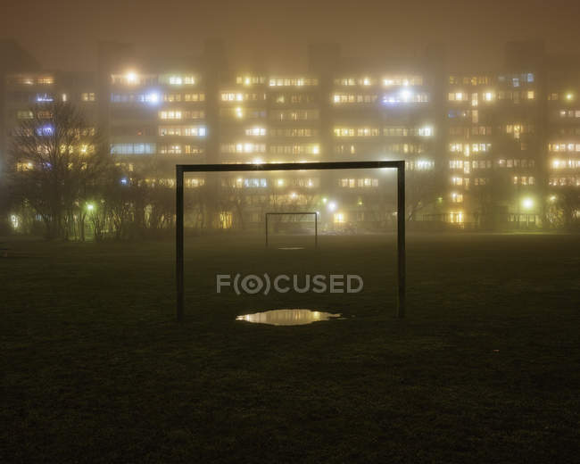 Bâtiments résidentiels éclairés avec terrain de football au premier plan dans le brouillard — Photo de stock