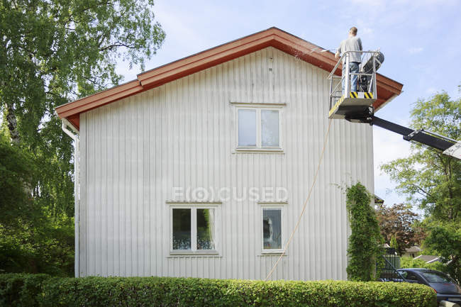 Rear view of man in cherry picker cleaning house — Stock Photo