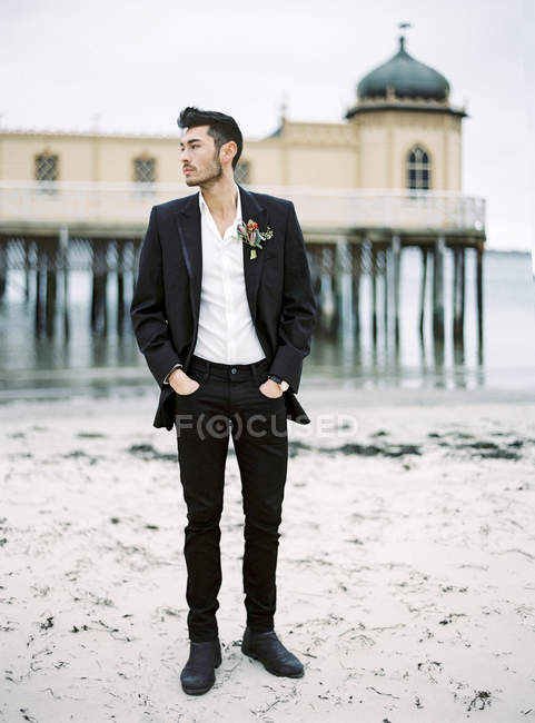 Jovem vestindo terno preto na praia de areia — Fotografia de Stock