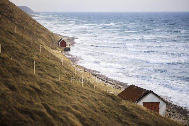 Cabañas a lo largo de la costa por mar con olas de surf - foto de stock